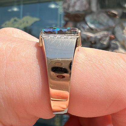 A men's gold boulder opal and diamond ring.  The opal shows blue and green colors.