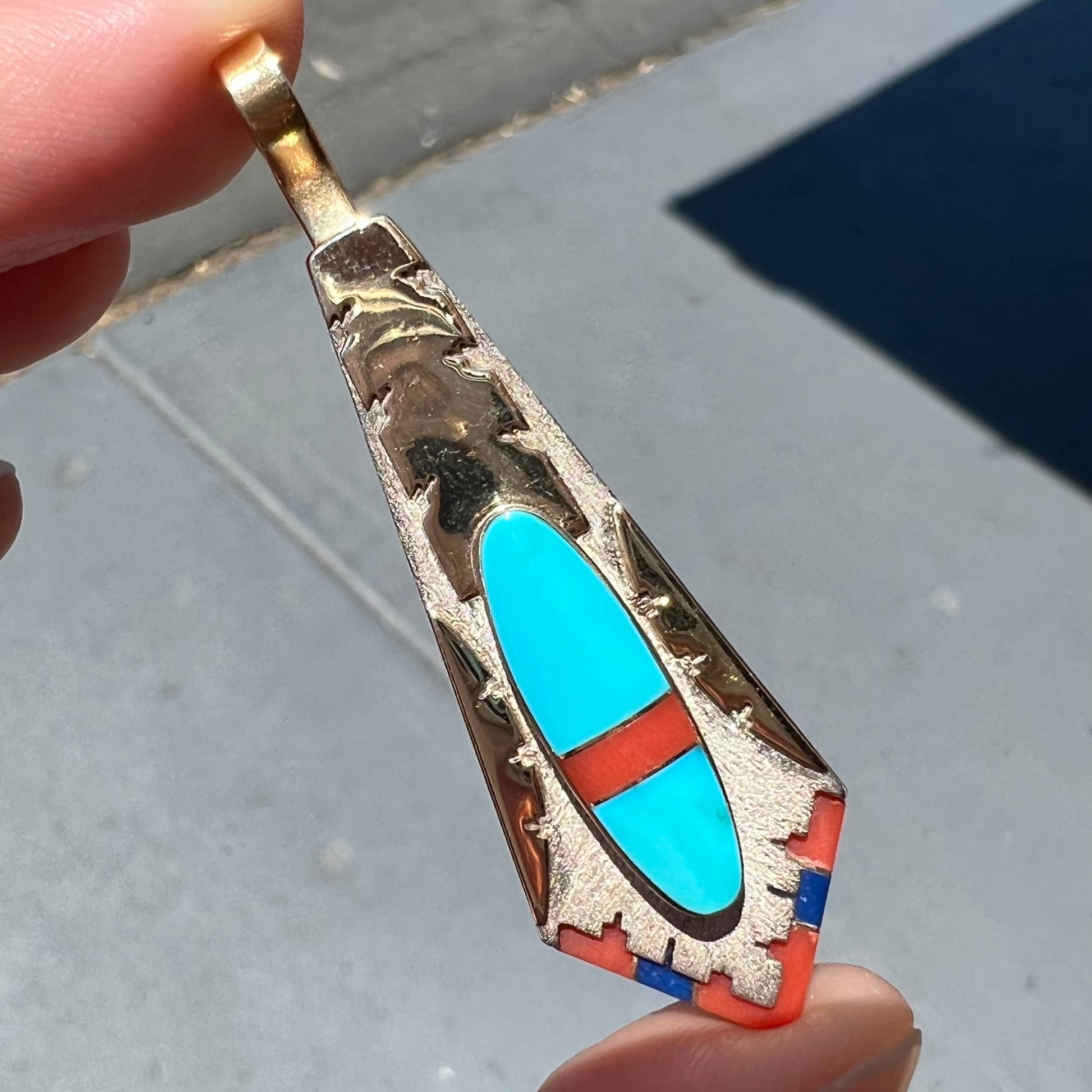 A yellow gold and sterling silver pendant inlaid with turquoise, coral, and lapis lazuli stones.  The piece is made by an unknown Native American artist and signed with the initials "LY".