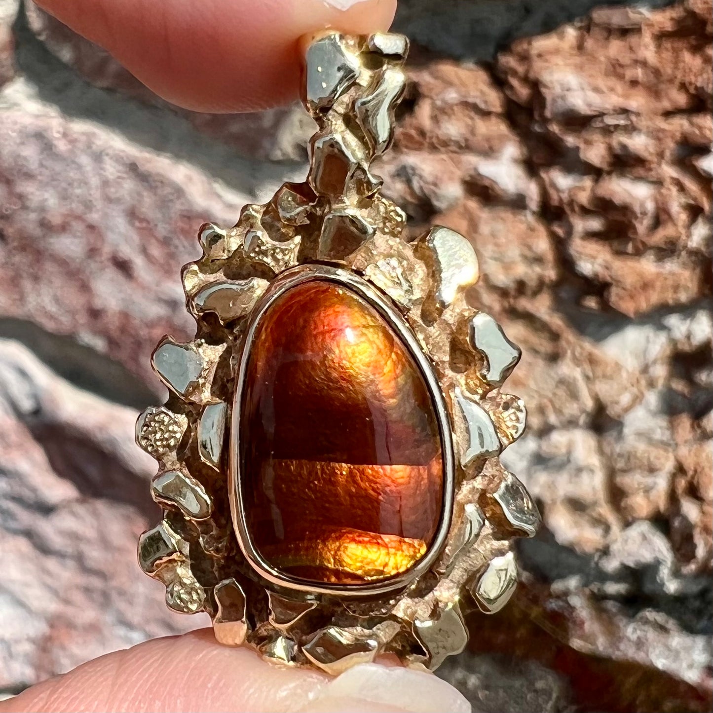 A gold nugget style pendant set with a freeform cabochon cut fire agate stone.