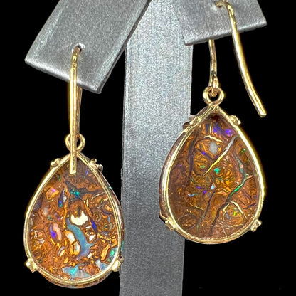 A pair of ladies' yellow gold dangle earrings set with pear shaped natural boulder opal stones from Koroit, Australia.