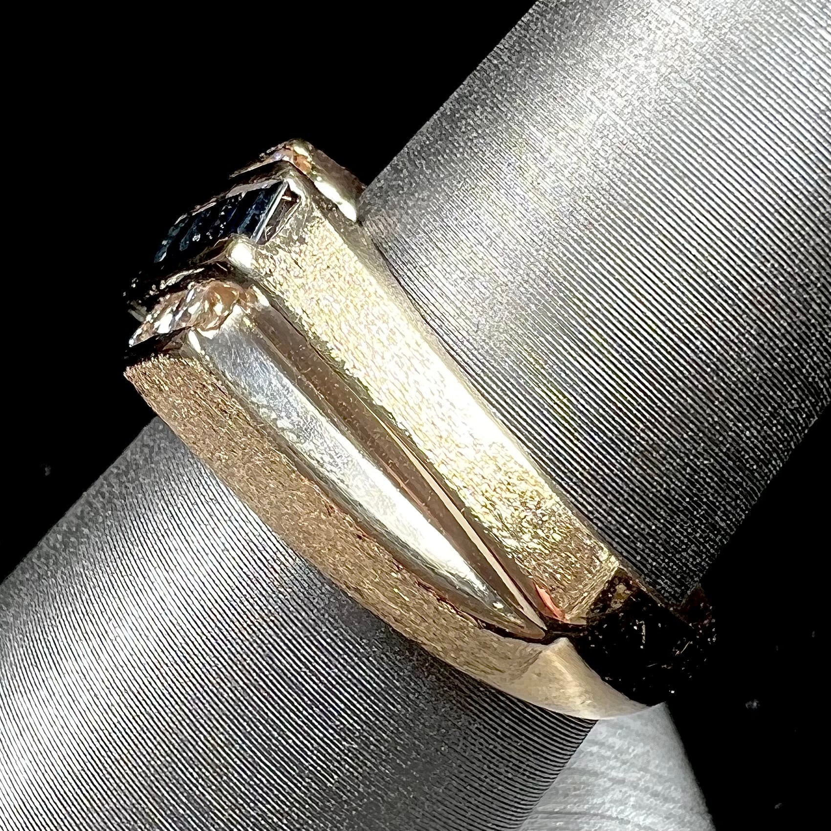 A men's yellow gold ring channel set with princess cut blue sapphires and diamonds.