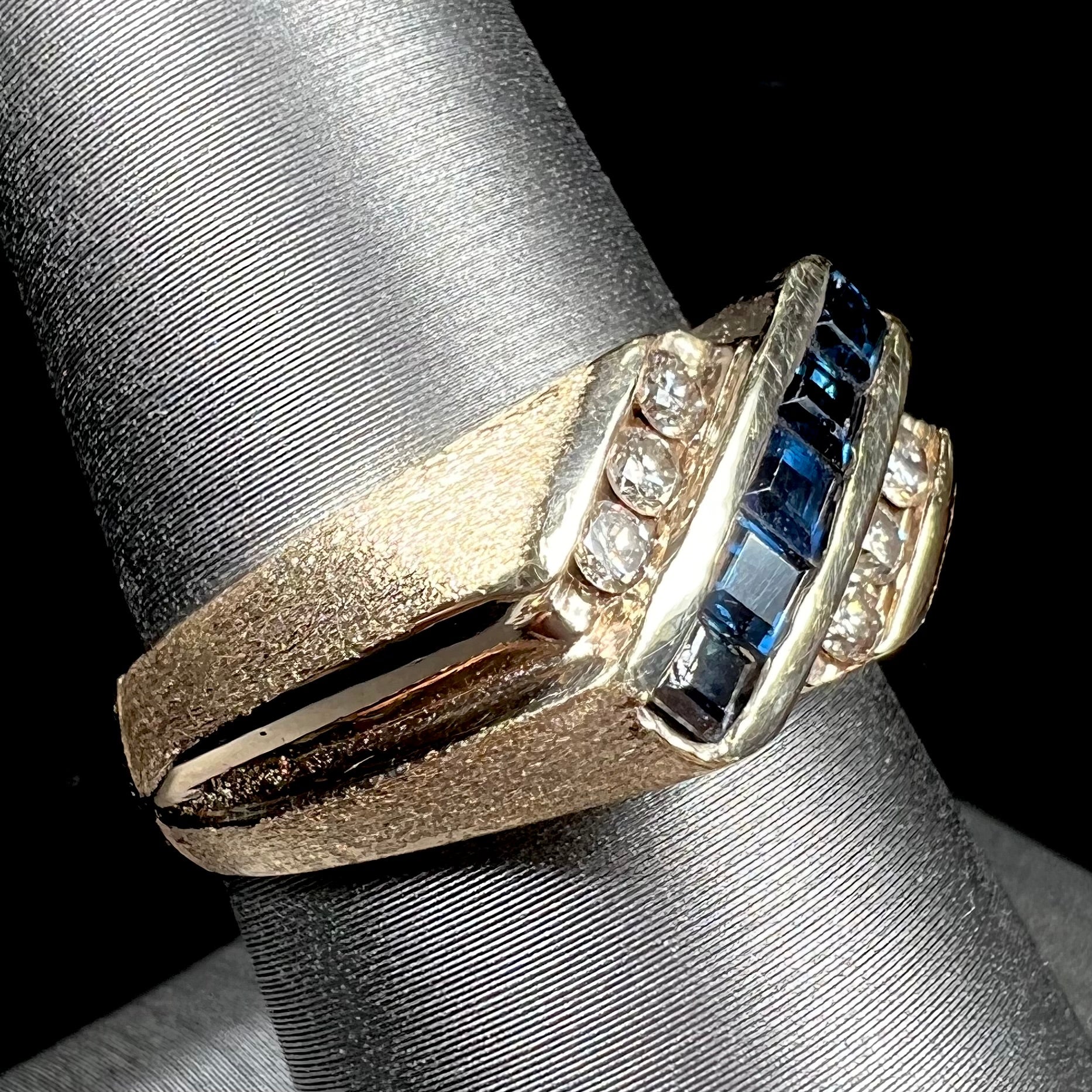 A men's yellow gold ring channel set with princess cut blue sapphires and diamonds.