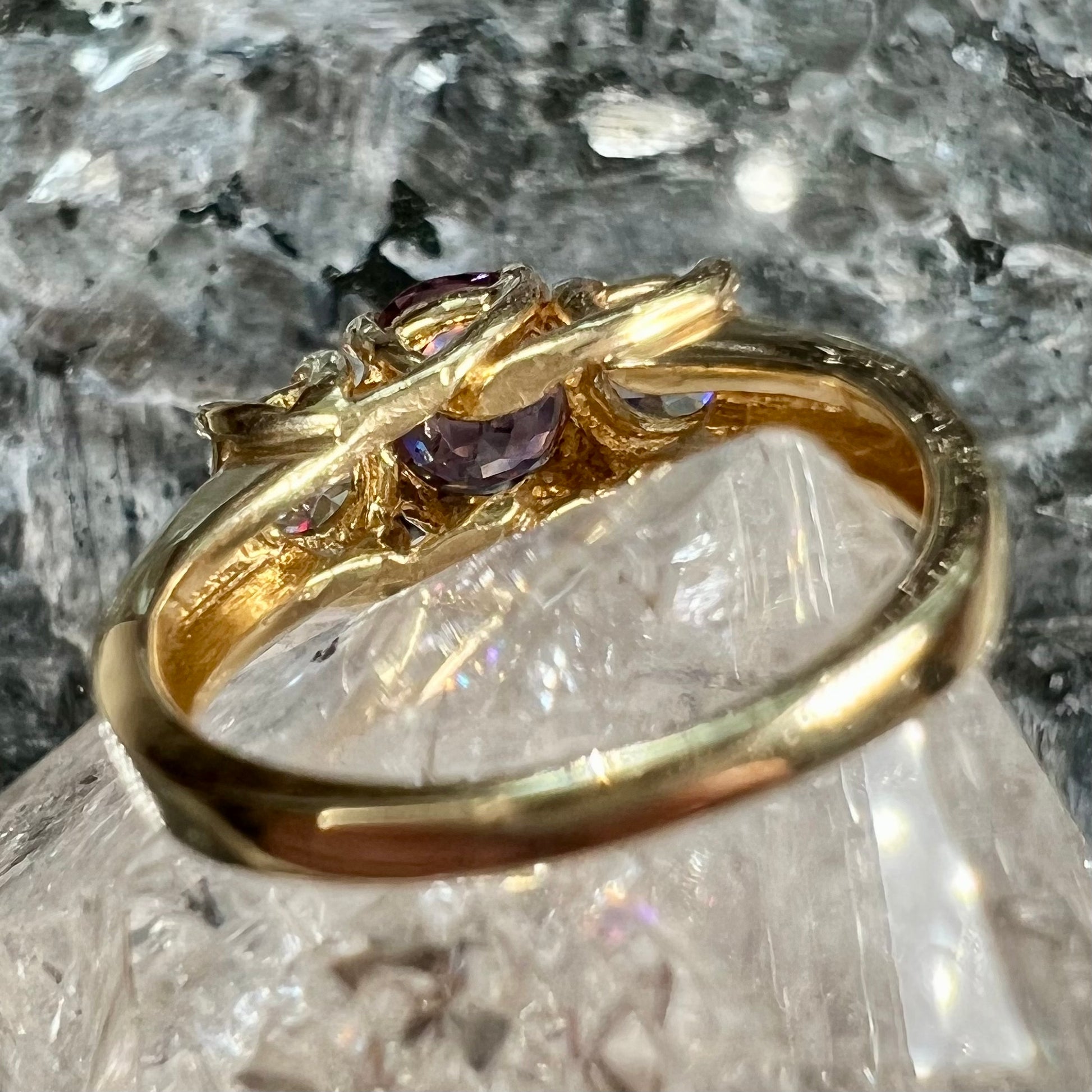 A yellow gold three stone ring set with two round cut white zircons and one cushion cut purple spinel.