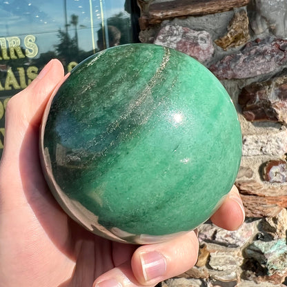 A stone sphere carved from natural green aventurine quartz with containing mica inclusions.