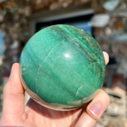 A stone sphere carved from natural green aventurine quartz with containing mica inclusions.