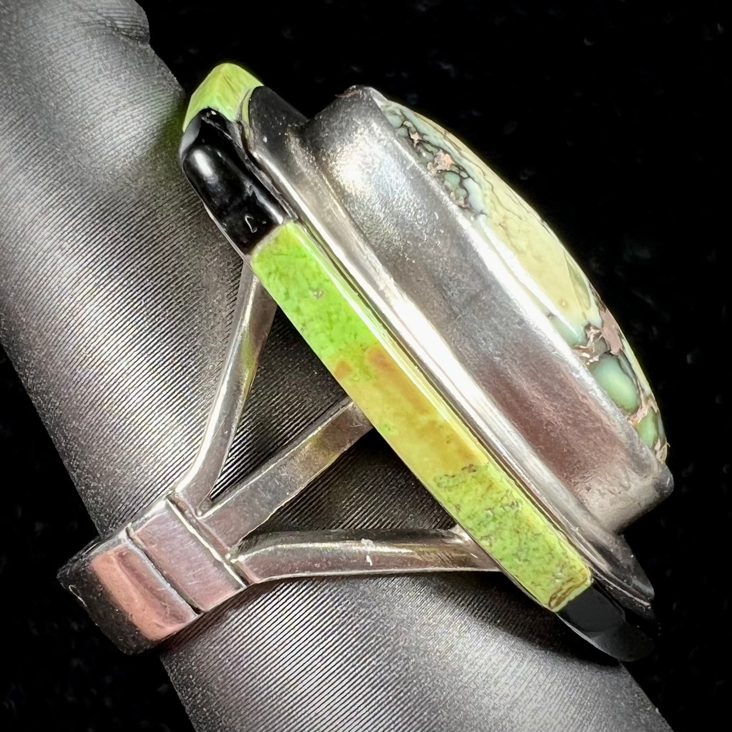 A shield shaped silver ring bezel set with a green gaspeite stone with stone inlaid edges, handmade by artist Benny Armijo.