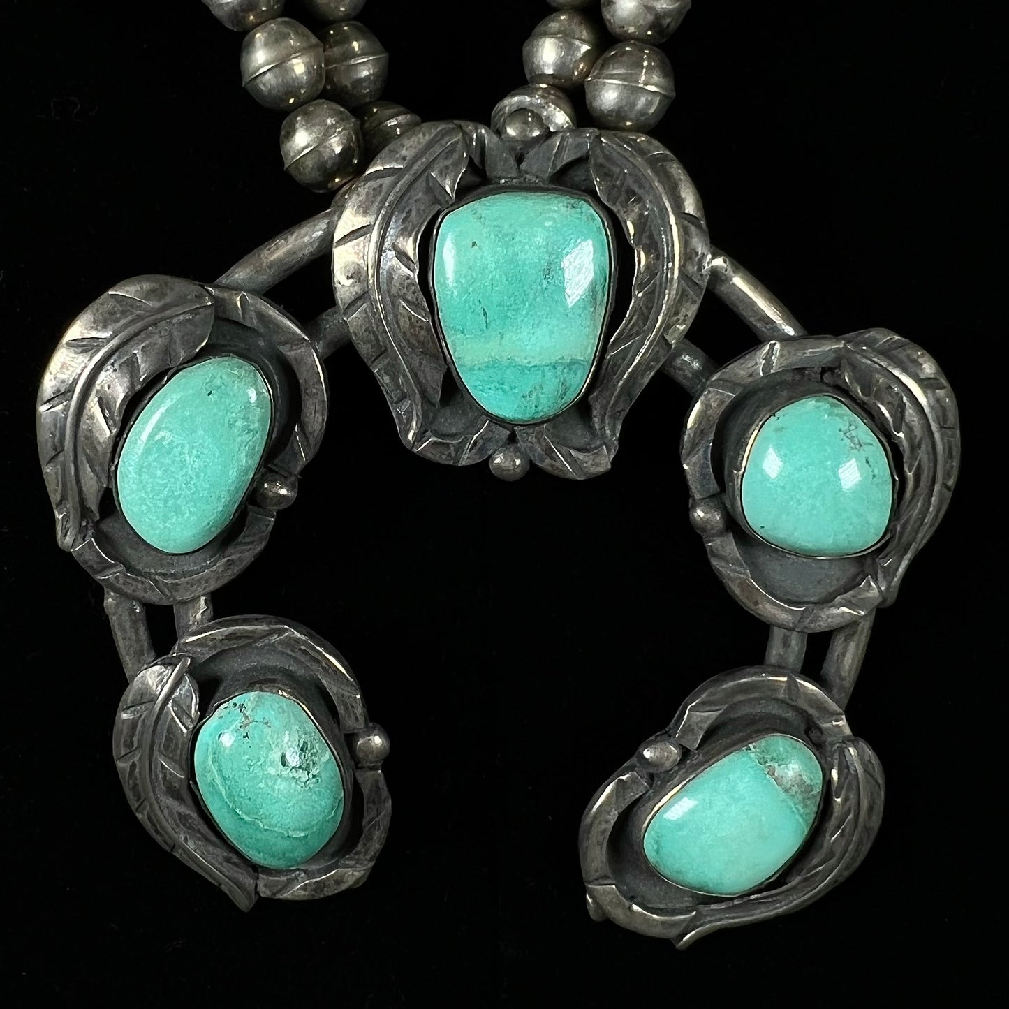 A handmade silver Navajo style squash blossom necklace set with green Kingman turquoise.