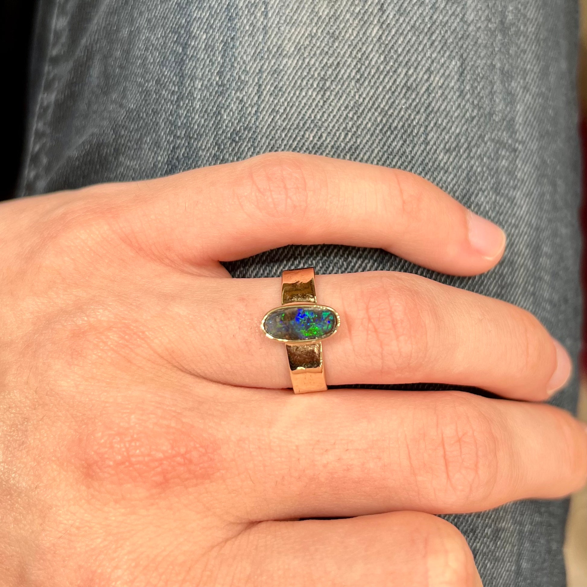 A blue green oval cabochon cut Australian boulder opal set in a yellow gold solitaire ring.
