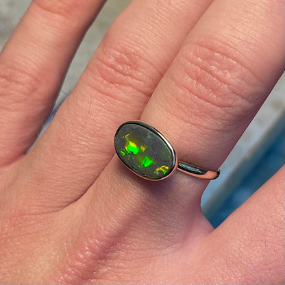 A handmade Lightning Ridge black opal solitaire ring in yellow gold.  Fire is green.