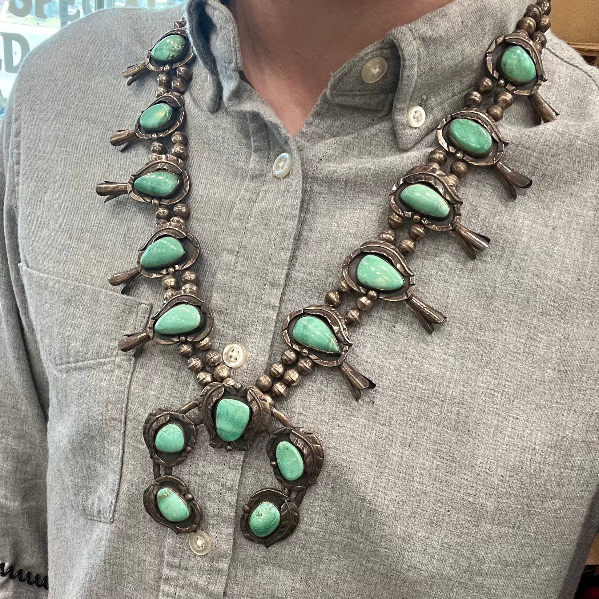 A handmade silver Navajo style squash blossom necklace set with green Kingman turquoise.
