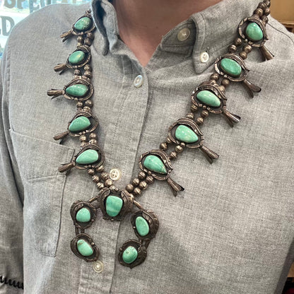 A handmade silver Navajo style squash blossom necklace set with green Kingman turquoise.