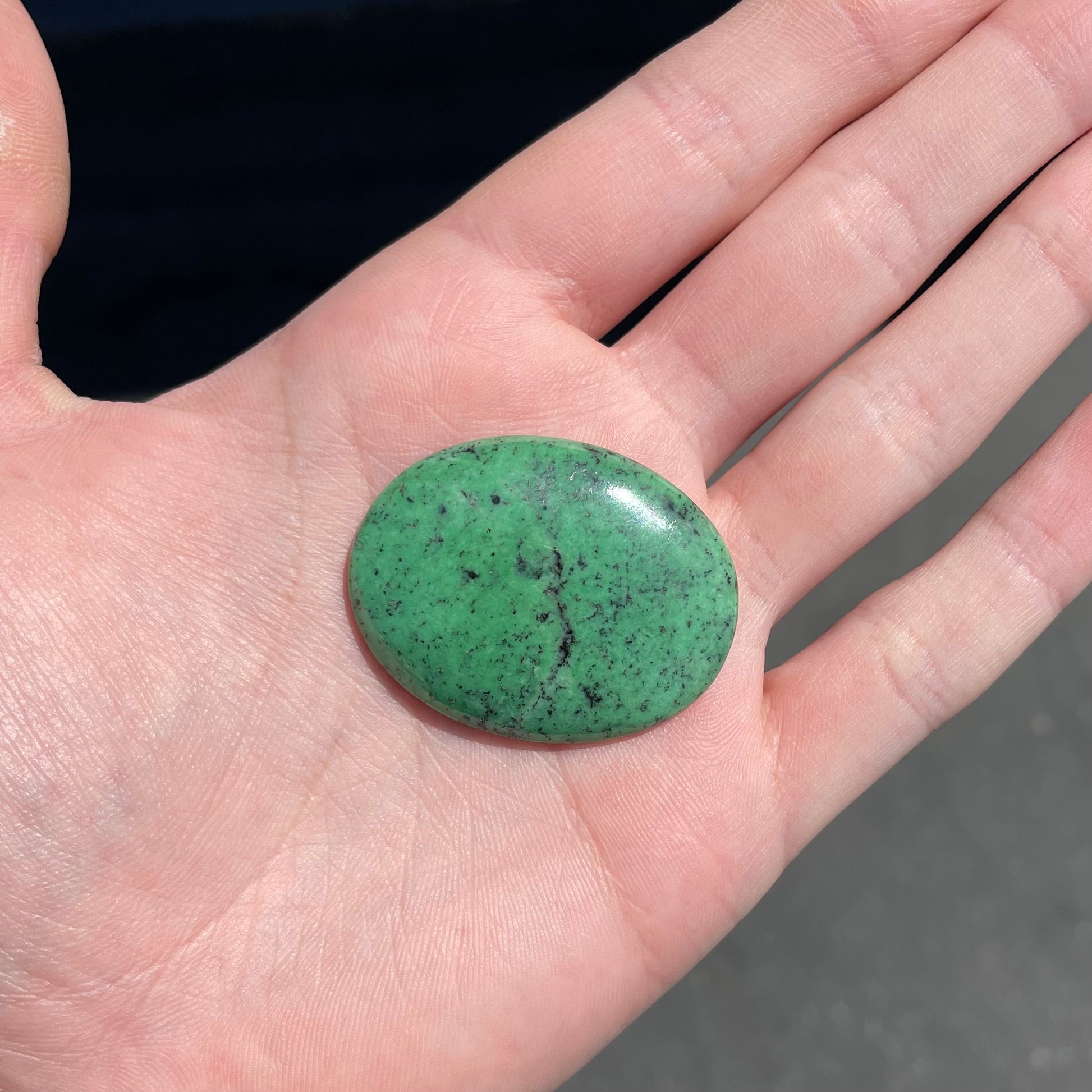 A loose, oval cabochon cut green zoisite stone with black spots.