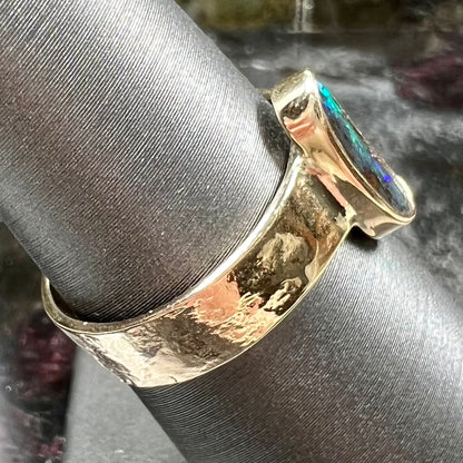 A blue green oval cabochon cut Australian boulder opal set in a yellow gold solitaire ring.