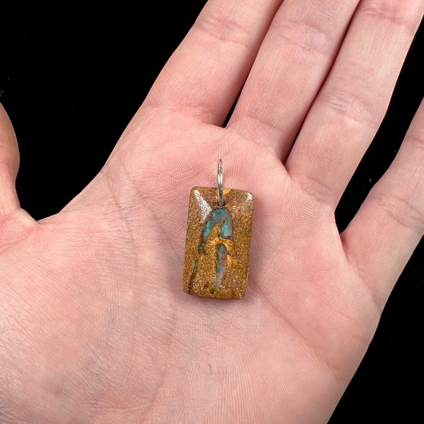 A drilled boulder opal stone with a sterling silver ring through the hole to be worn as a pendant.  The pattern resembles a hamsa hand.