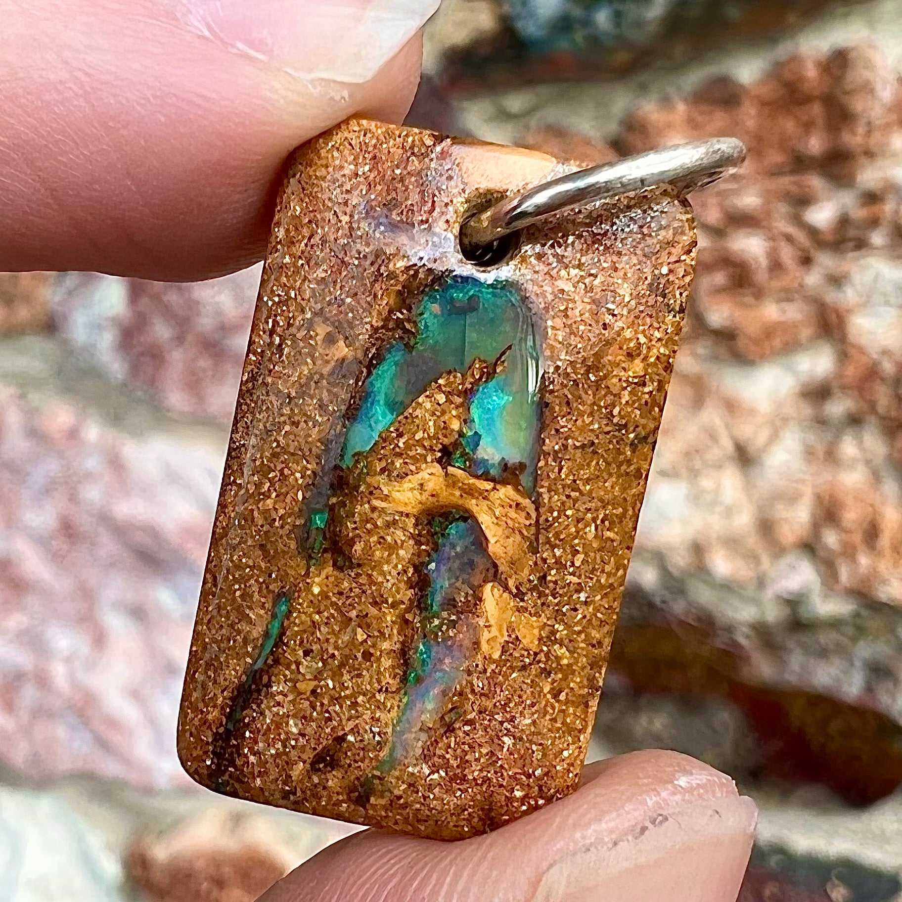 A drilled boulder opal stone with a sterling silver ring through the hole to be worn as a pendant.  The pattern resembles a hamsa hand.