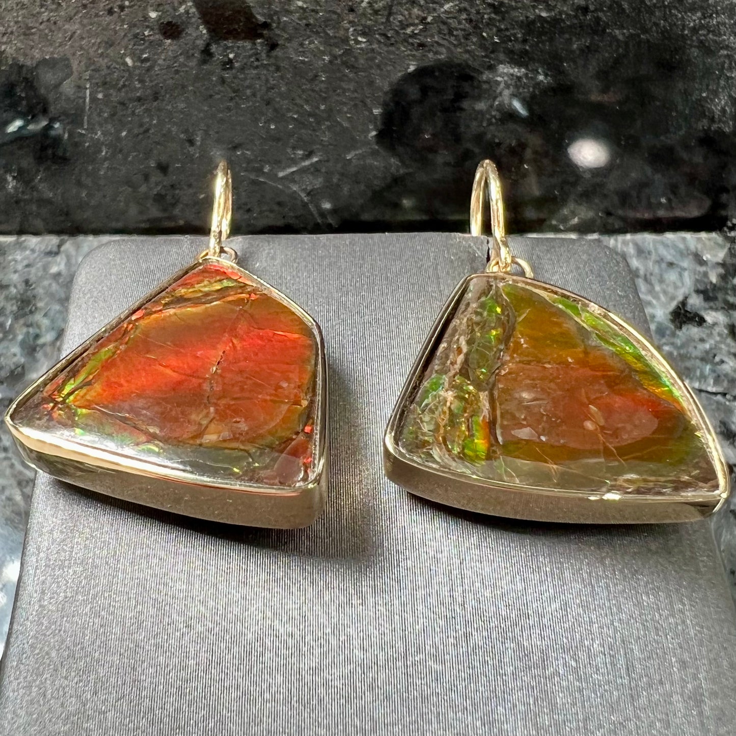 Yellow gold French wire dangle earrings bezel set with two polished freeform cut red ammolite fossils.