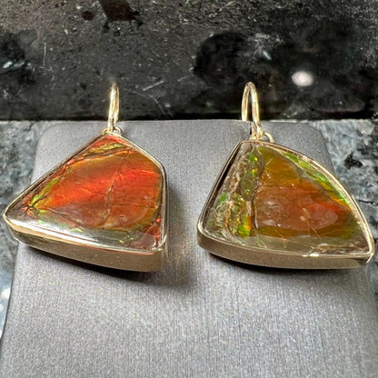 Yellow gold French wire dangle earrings bezel set with two polished freeform cut red ammolite fossils.