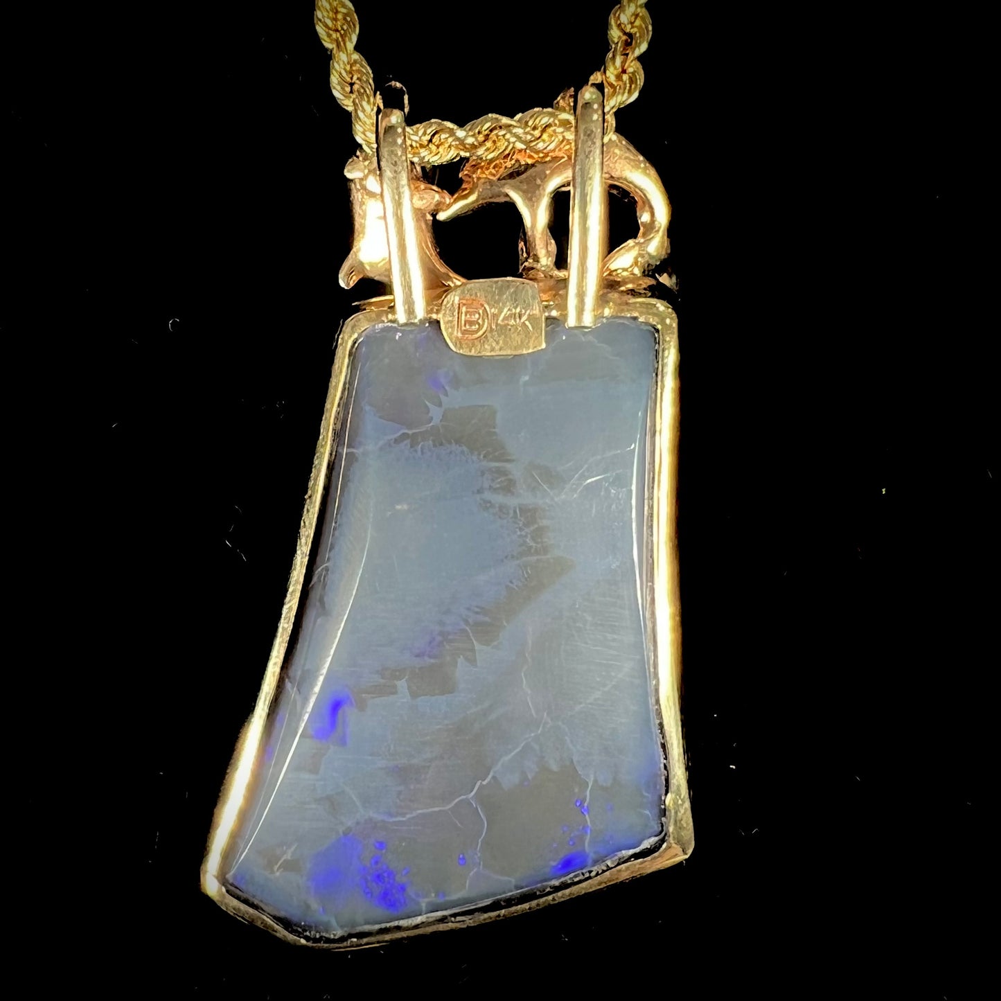 A gold freeform cut black opal bezel pendant cast with two dolphins on top of the opal.