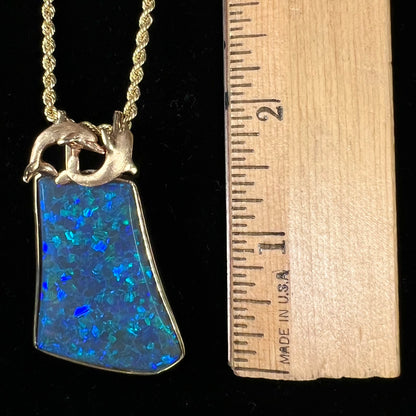 A gold freeform cut black opal bezel pendant cast with two dolphins on top of the opal.