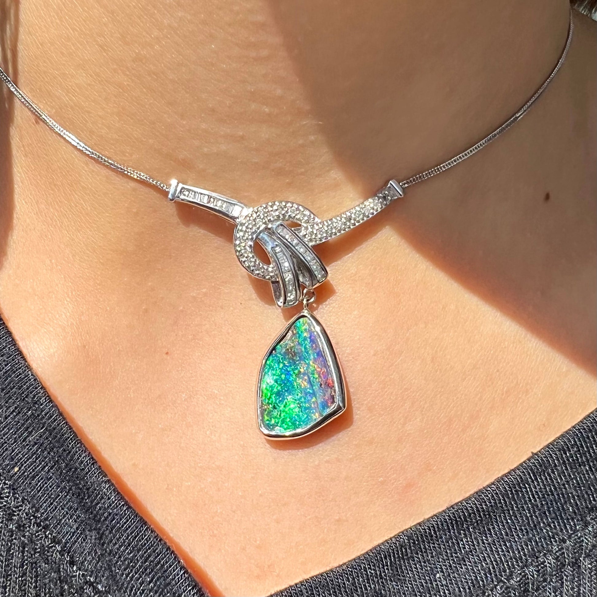 A white gold necklace set with diamonds and a dangling, bezel set boulder opal.