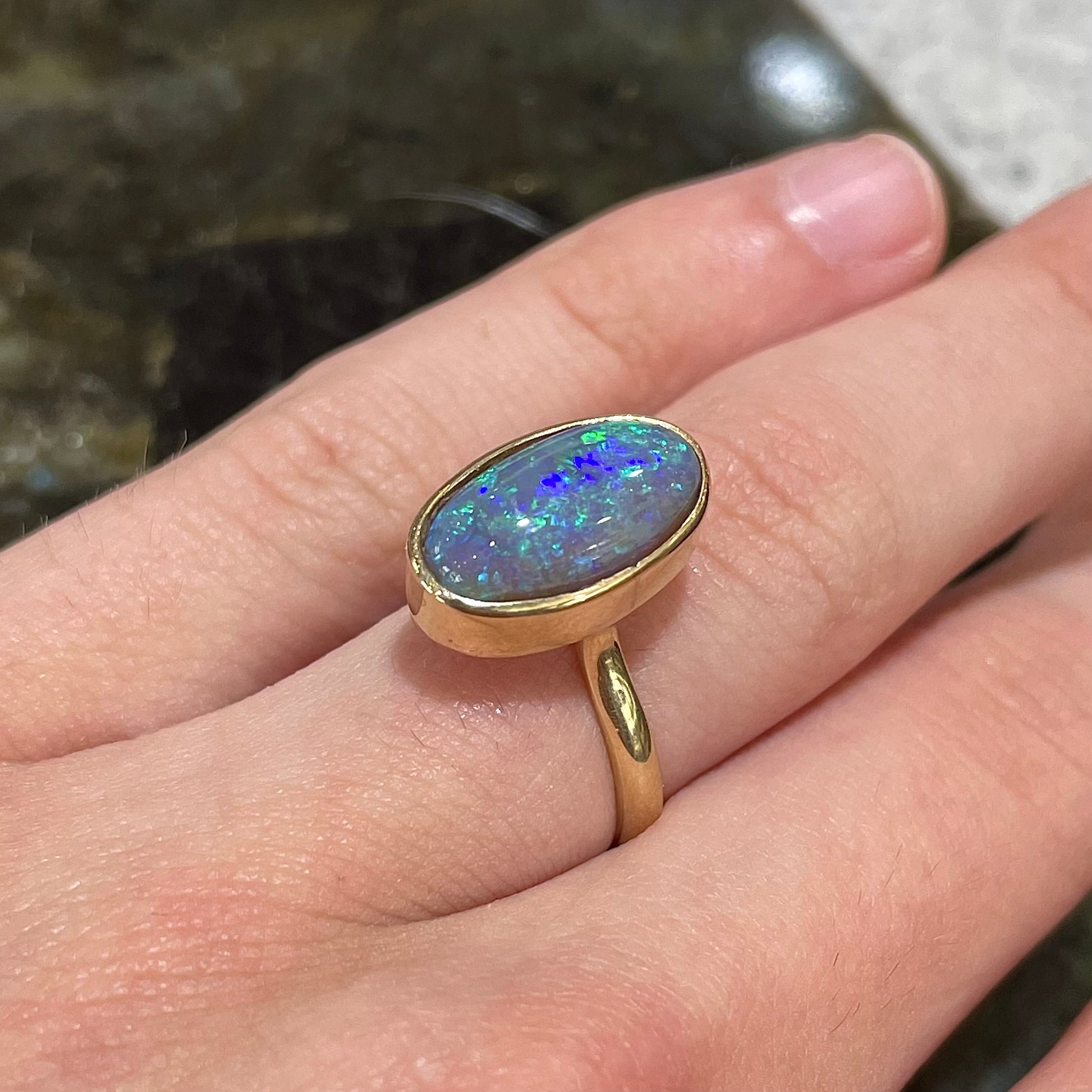 A simple yellow gold solitaire ring with a bezel set Lightning Ridge black crystal opal from Australia.