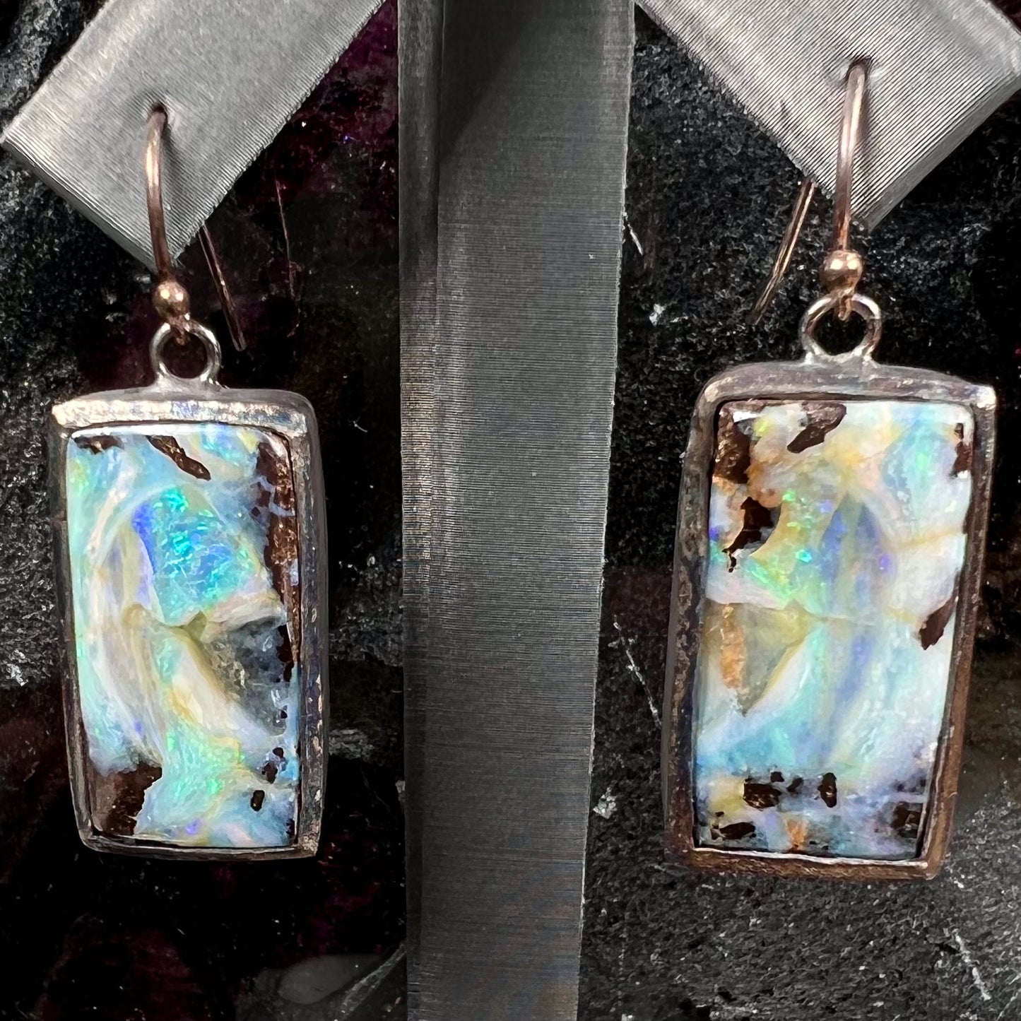 A pair of handmade sterling silver boulder opal earrings.  The earrings dangle from French wire hooks.