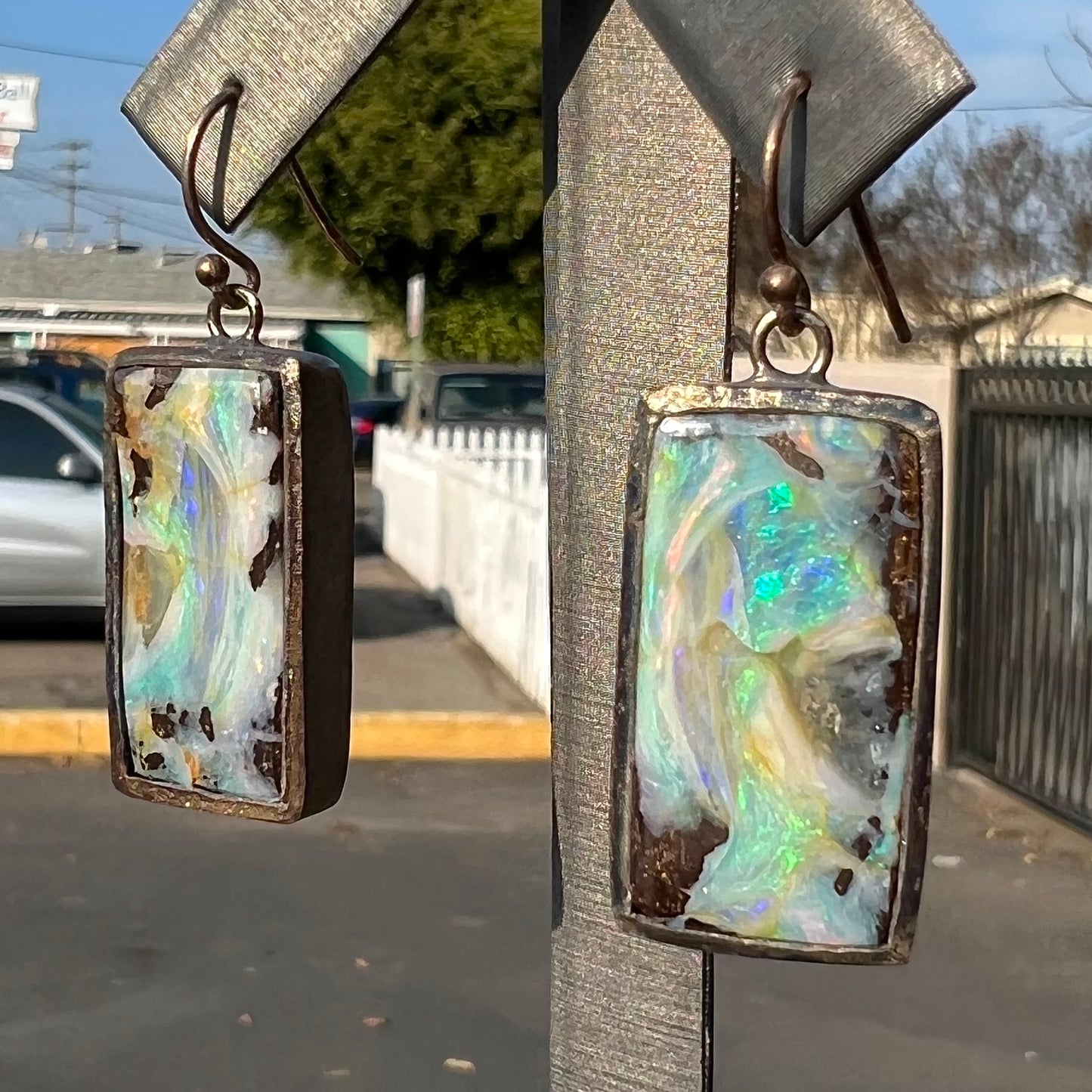 A pair of handmade sterling silver boulder opal earrings.  The earrings dangle from French wire hooks.