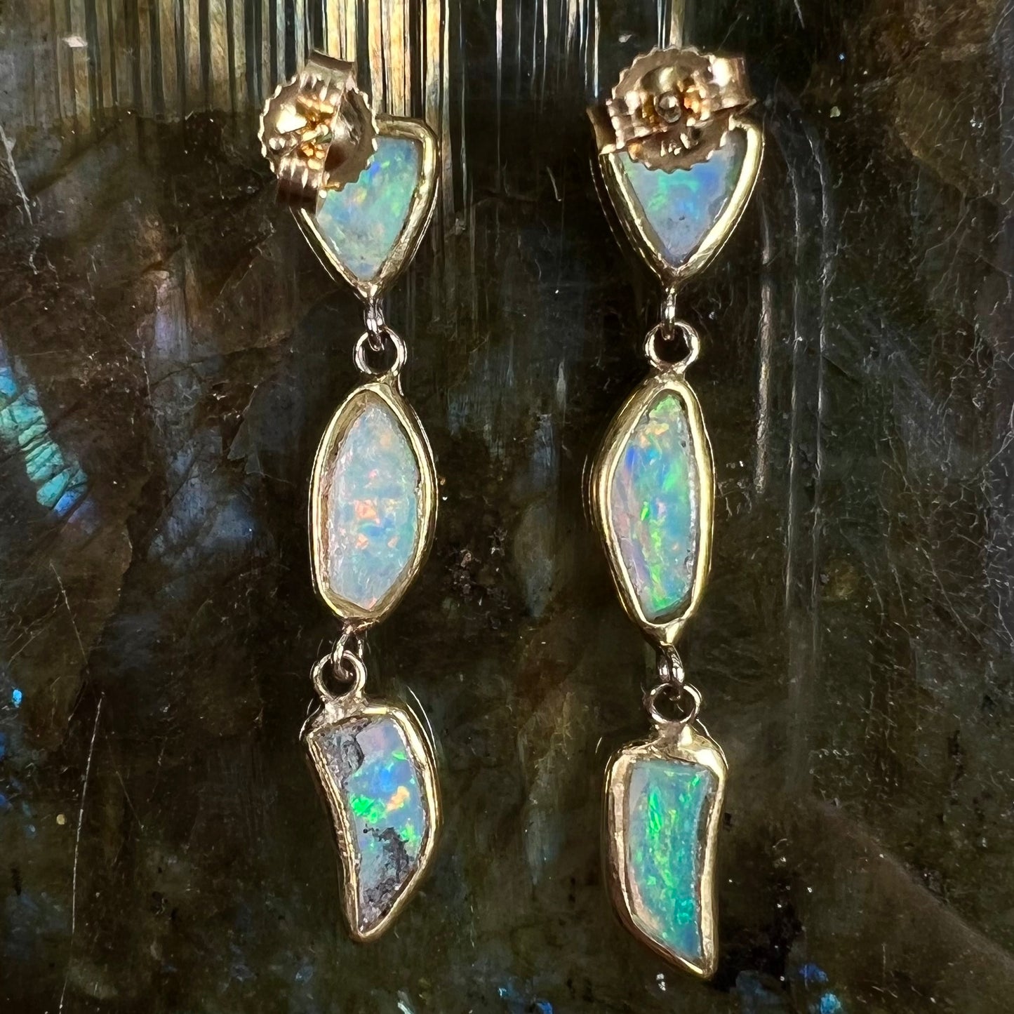 A pair of yellow gold push-back dangle earrings set with three white crystal opals in each.
