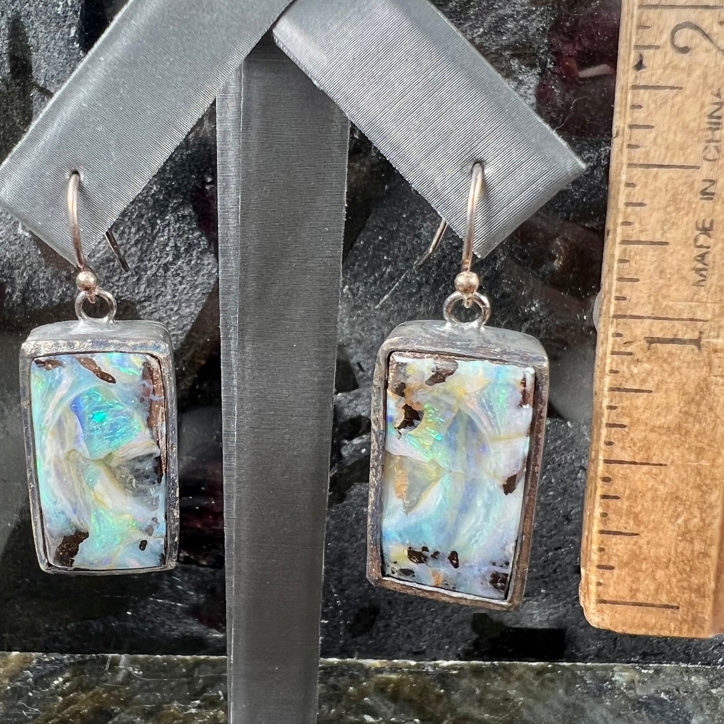 A pair of handmade sterling silver boulder opal earrings.  The earrings dangle from French wire hooks.