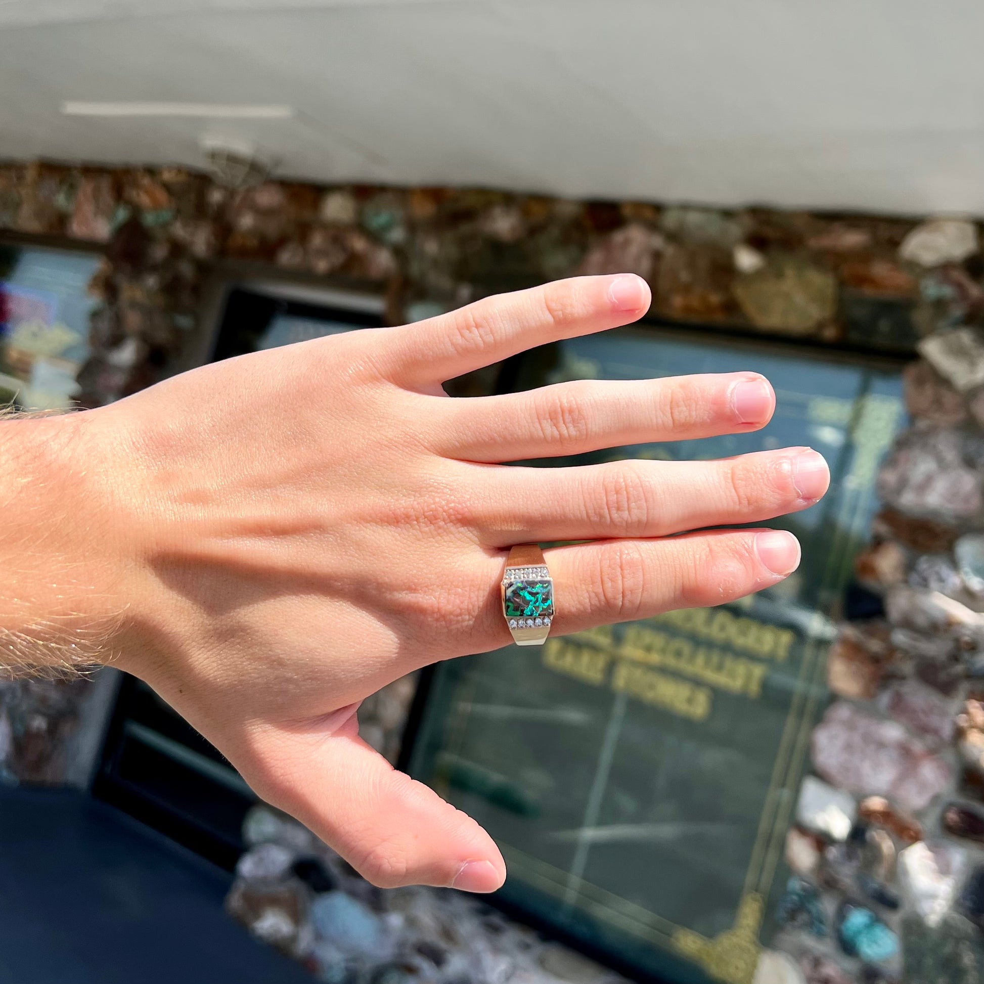 A men's gold boulder opal and diamond ring.  The opal shows blue and green colors.