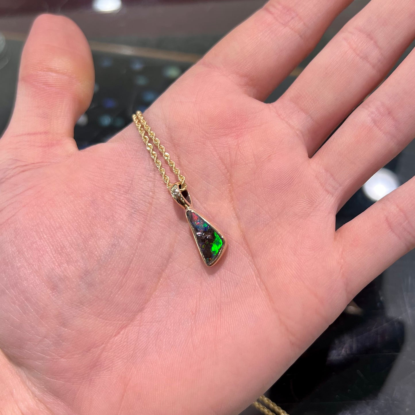 A bright green and red boulder opal bezel pendant in solid yellow gold.