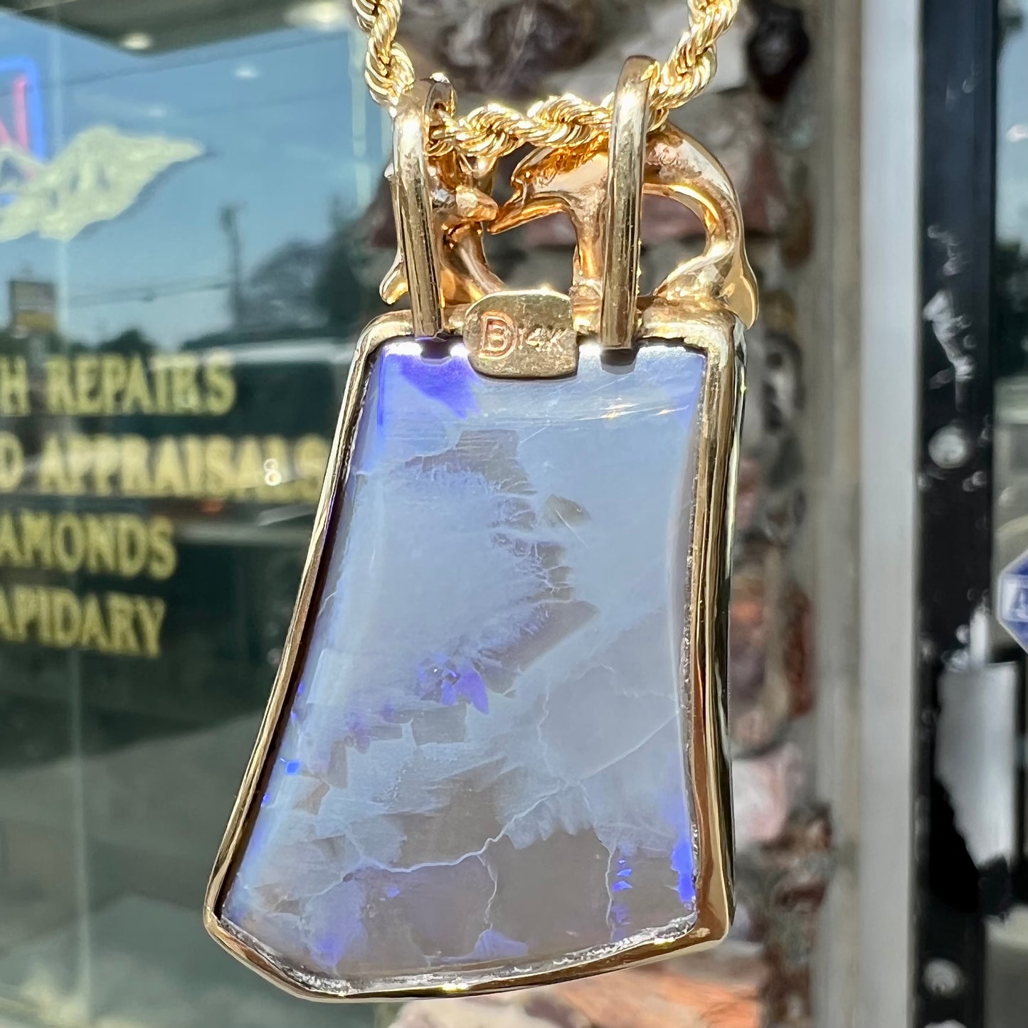 A gold freeform cut black opal bezel pendant cast with two dolphins on top of the opal.