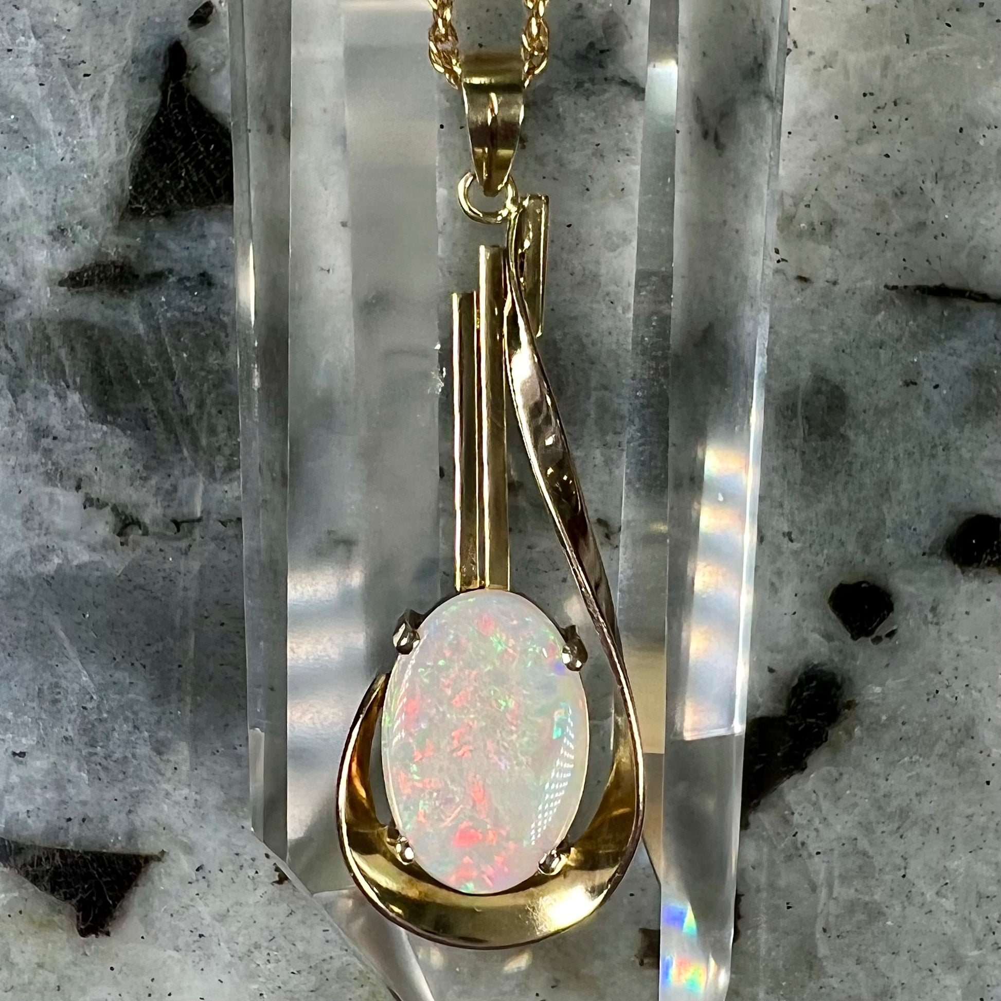 A handmade gold drop pendant set with an oval cabochon cut white crystal opal.
