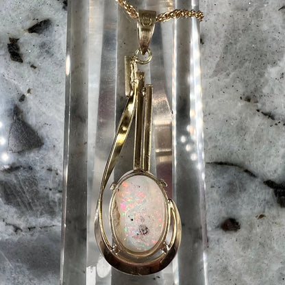 A handmade gold drop pendant set with an oval cabochon cut white crystal opal.