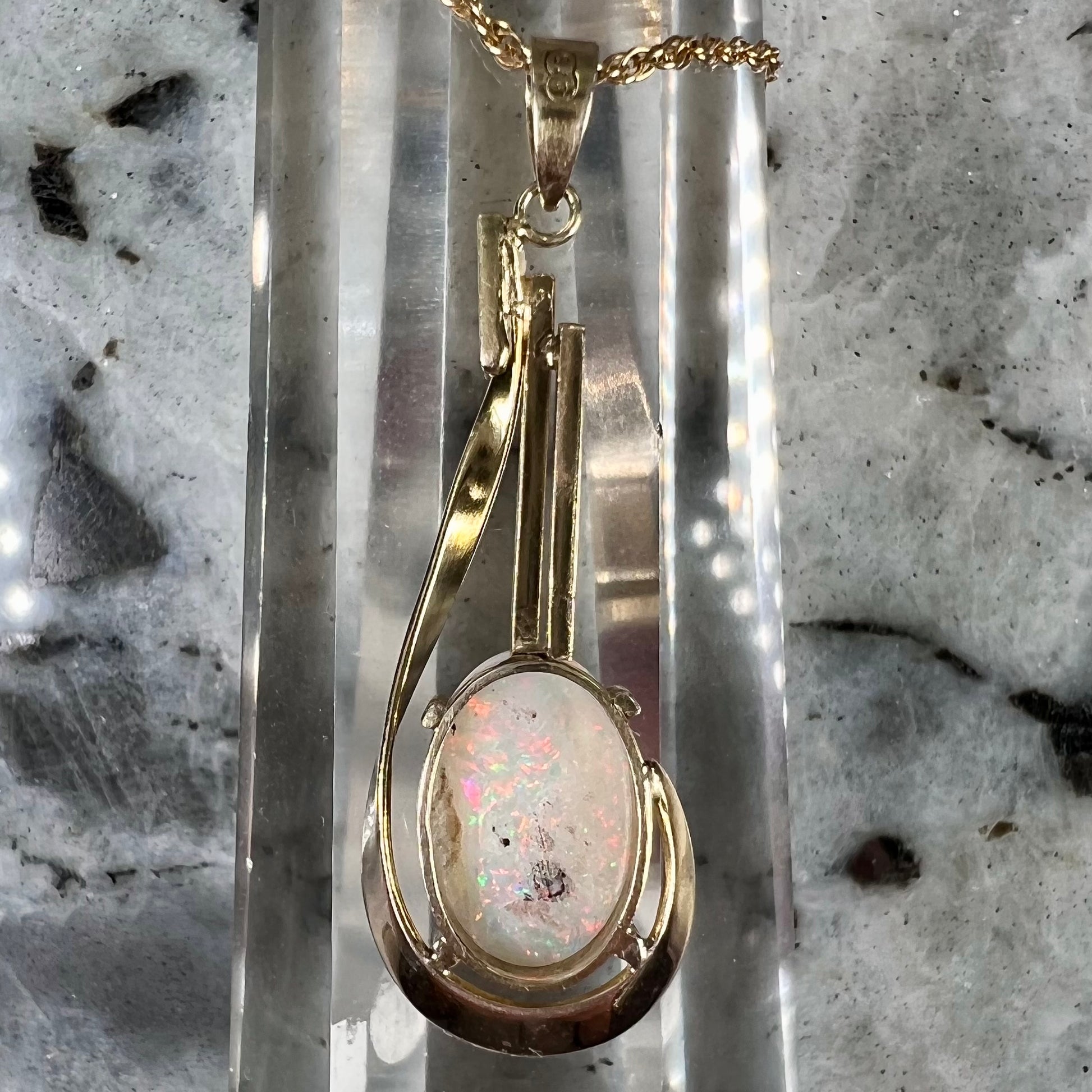 A handmade gold drop pendant set with an oval cabochon cut white crystal opal.