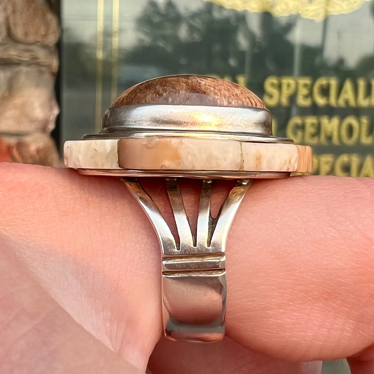 A silver ring handmade from a bezel set petrified wood stone, surrounded by quartz, carnelian, and bone inlay.