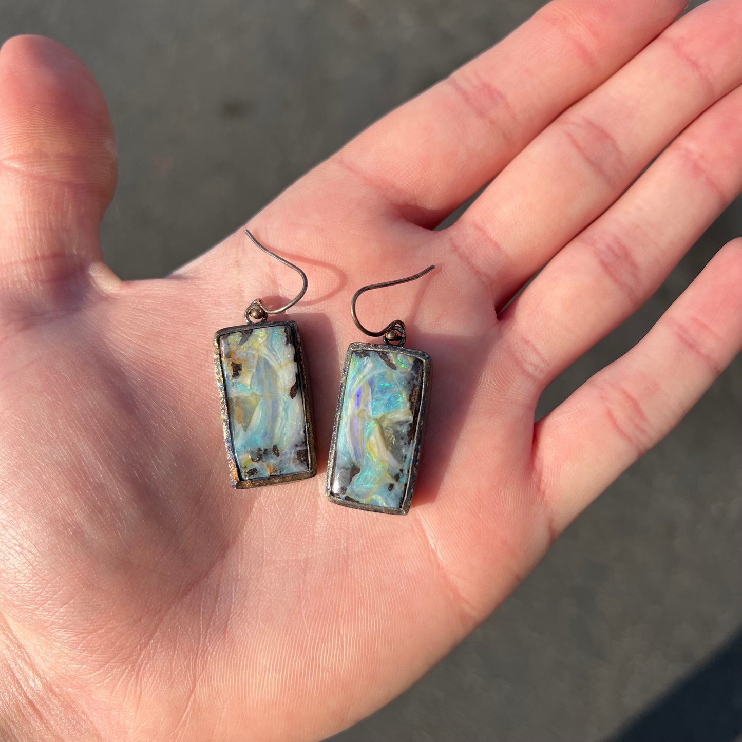 A pair of handmade sterling silver boulder opal earrings.  The earrings dangle from French wire hooks.