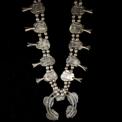 A handmade silver Navajo style squash blossom necklace set with green Kingman turquoise.