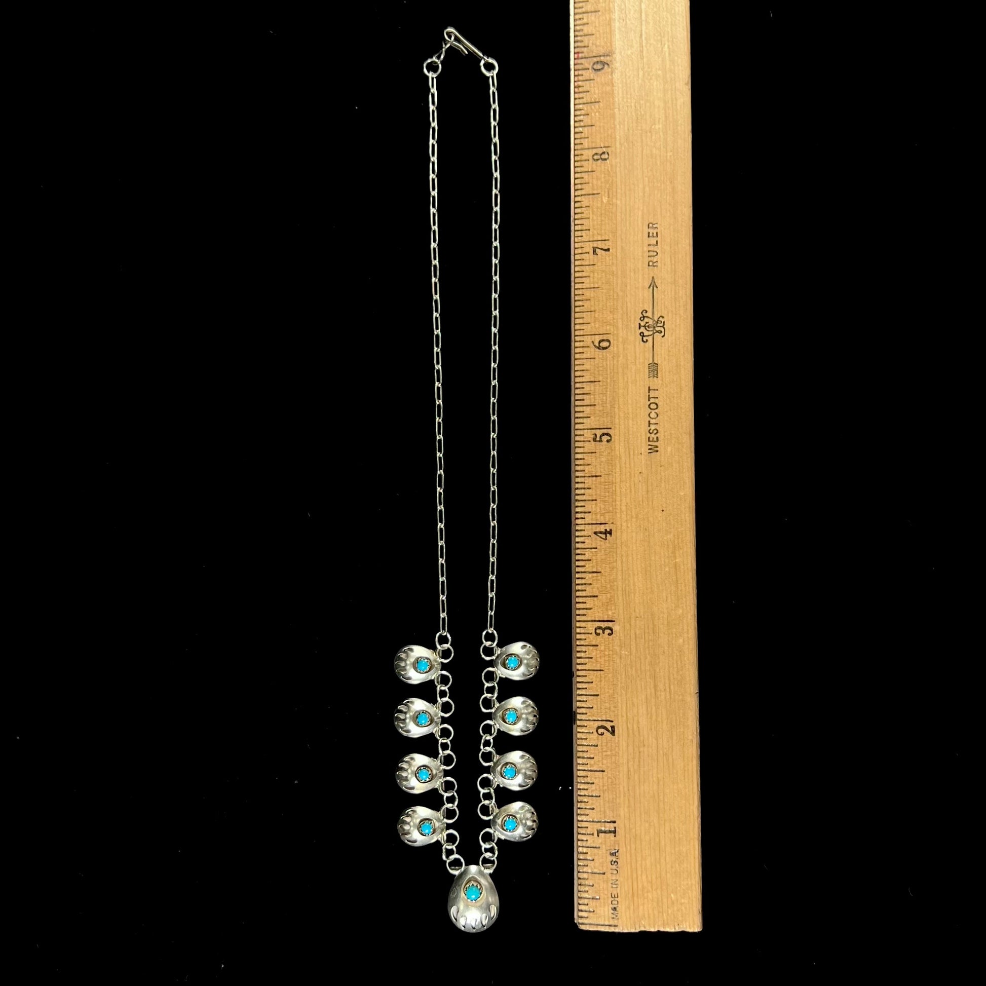 A silver turquoise necklace handmade with nine silver bear paws set with round turquoise stones.