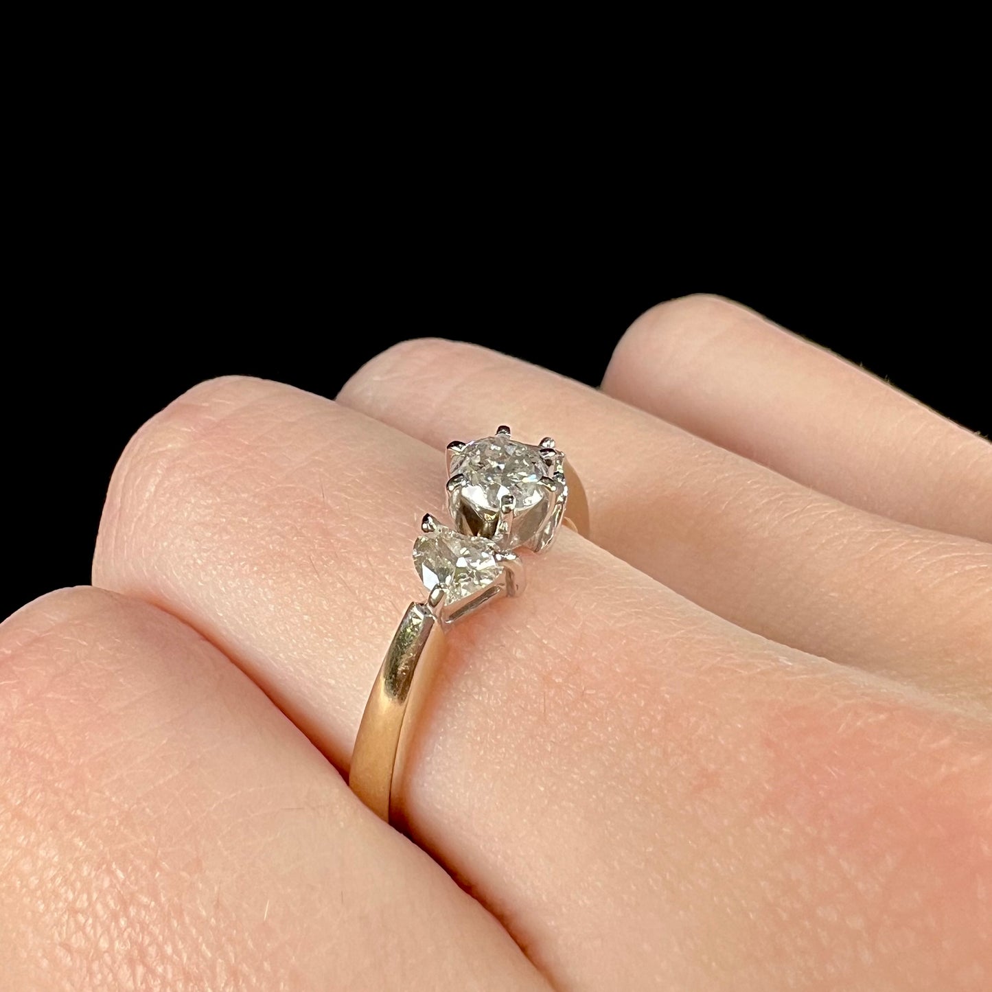 A ladies' three stone diamond ring.  The center diamond is a round brilliant cut, and the two accents are heart shaped diamonds.