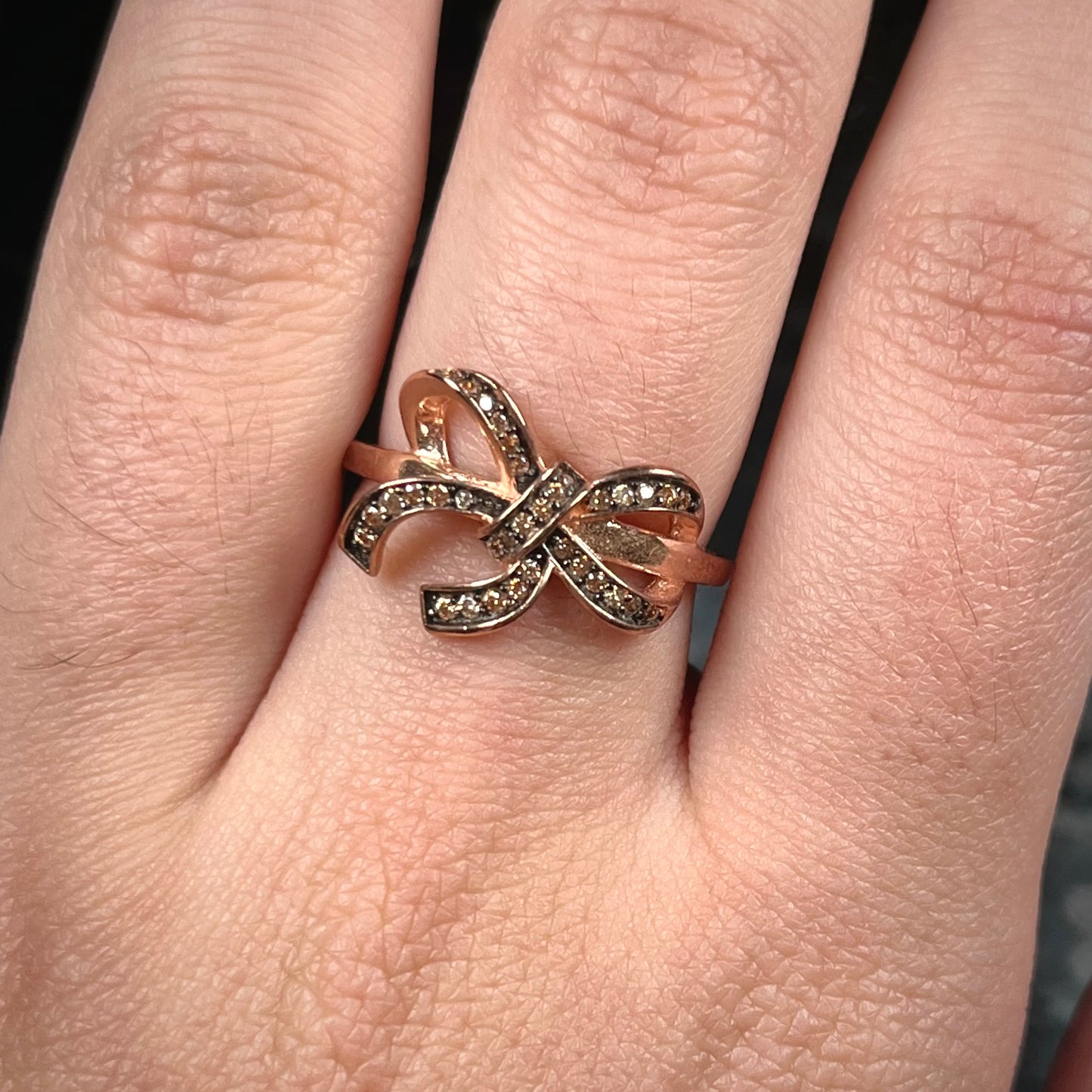 A rose gold colored bow ring.  The bow is tied in a knot, and the knot is set with cognac cubic zirconia.