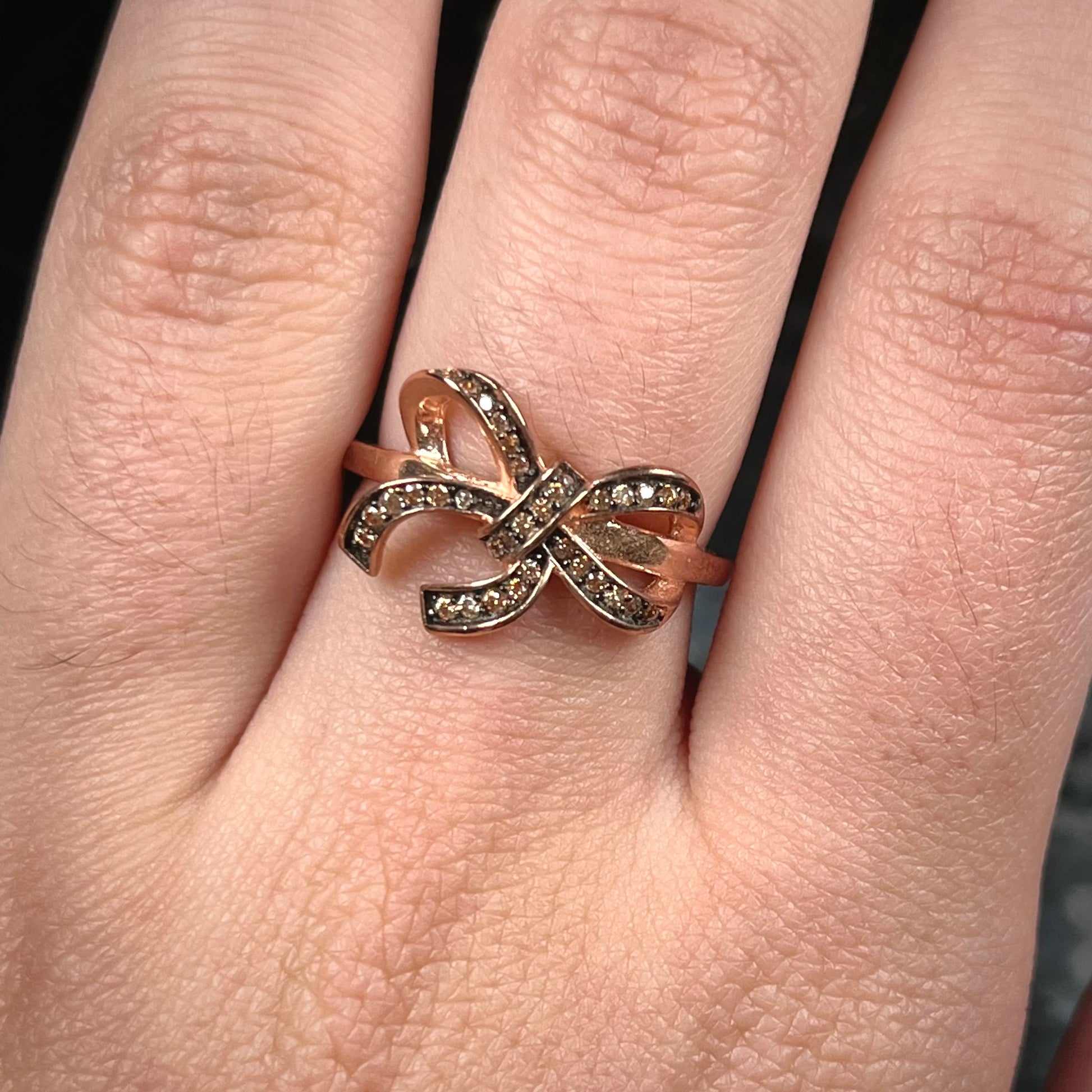 A rose gold colored bow ring.  The bow is tied in a knot, and the knot is set with cognac cubic zirconia.