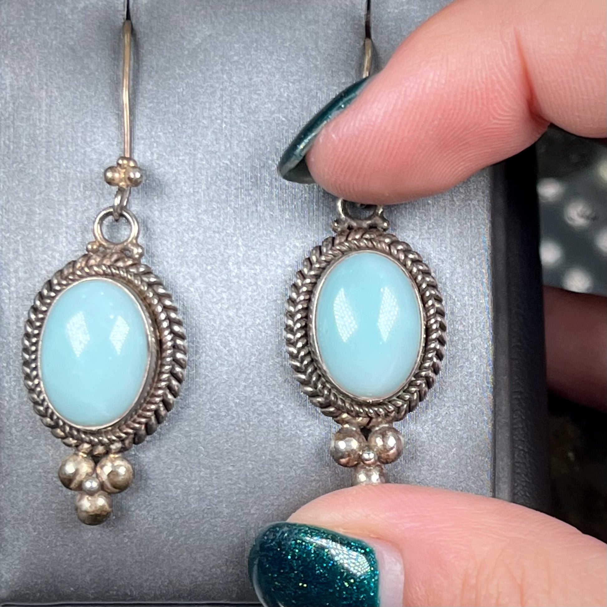 A pair of silver wire dangle earrings set with blue agate stones.  The earrings have a braided rope design.