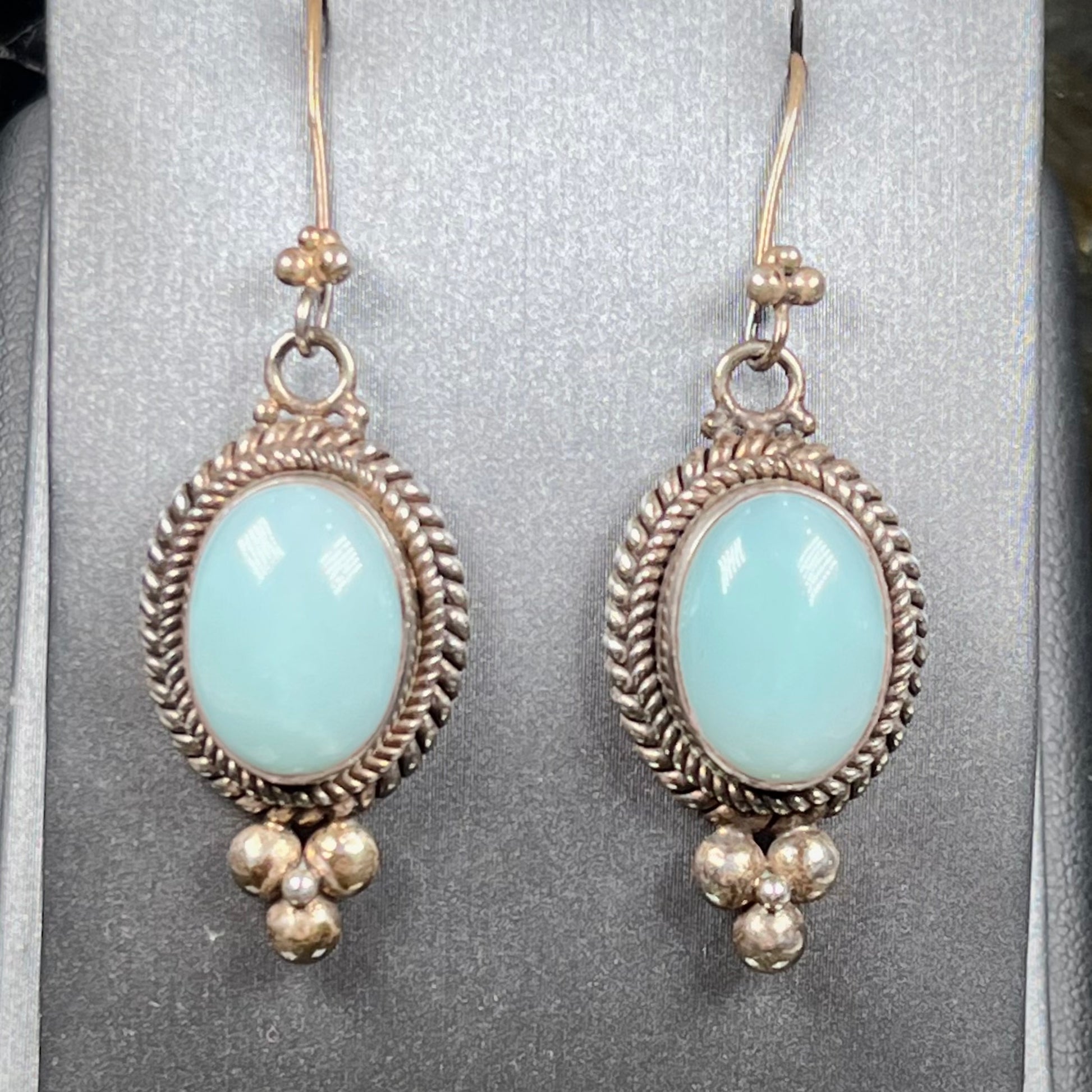 A pair of silver wire dangle earrings set with blue agate stones.  The earrings have a braided rope design.