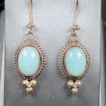 A pair of silver wire dangle earrings set with blue agate stones.  The earrings have a braided rope design.
