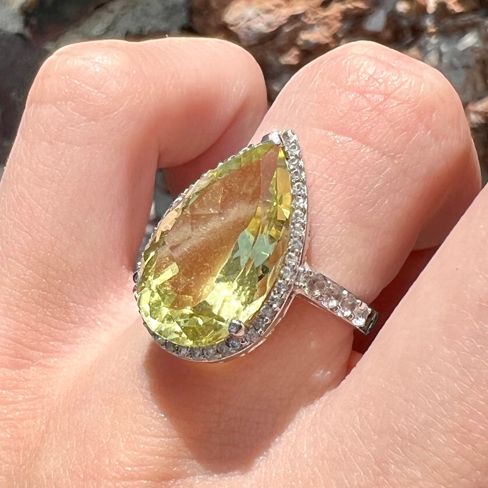 A pear shape lemon quartz set in a sterling silver and white topaz halo ring.