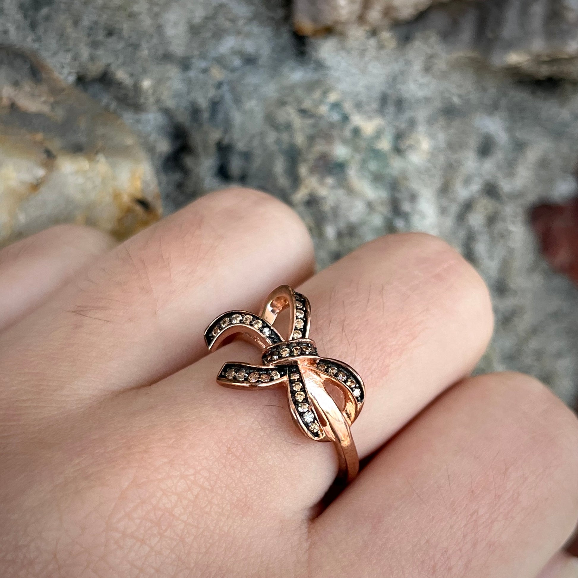 A rose gold colored bow ring.  The bow is tied in a knot, and the knot is set with cognac cubic zirconia.