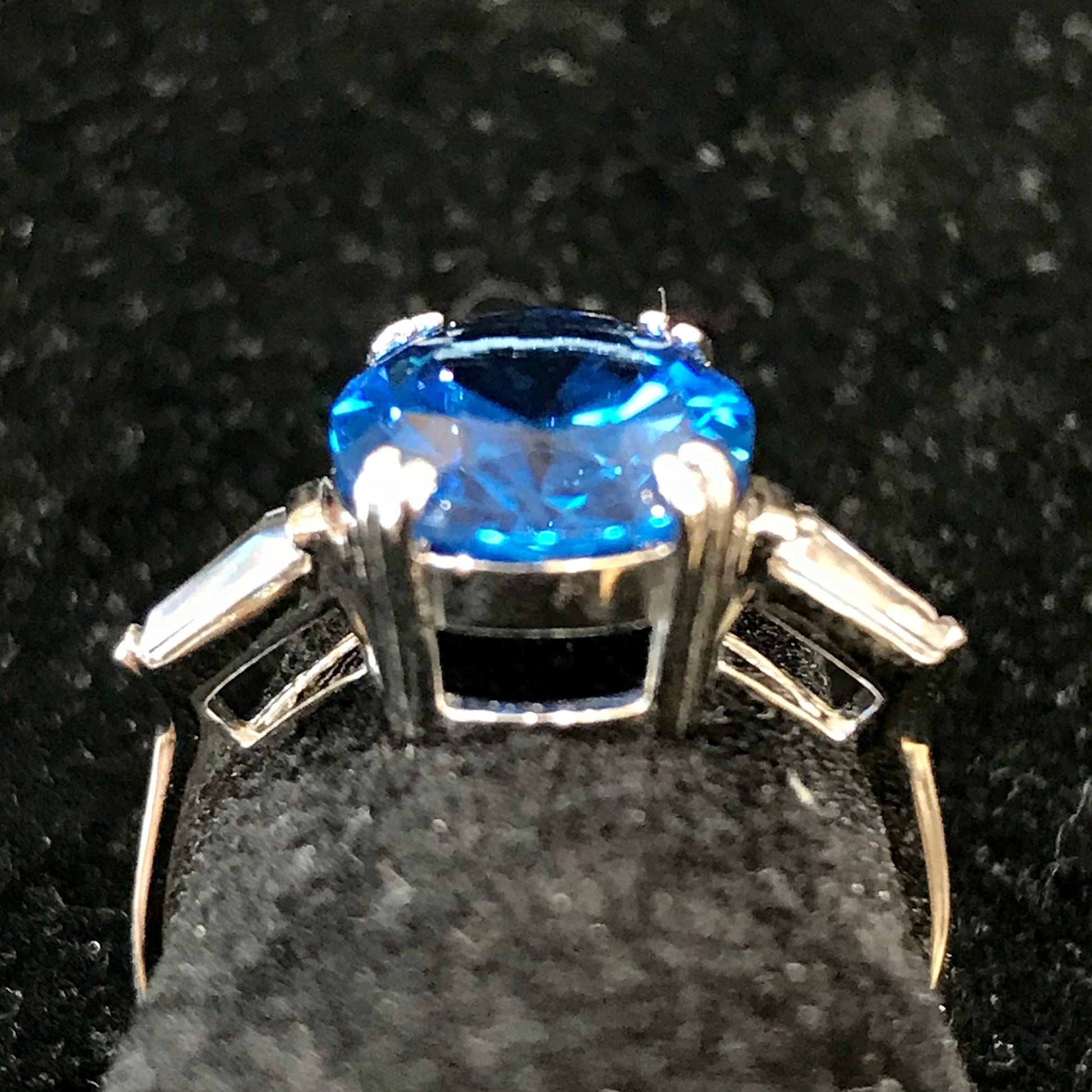 A sterling silver ring set with a faceted oval cut blue spinel and cubic zirconia baguettes.