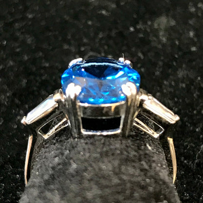 A sterling silver ring set with a faceted oval cut blue spinel and cubic zirconia baguettes.
