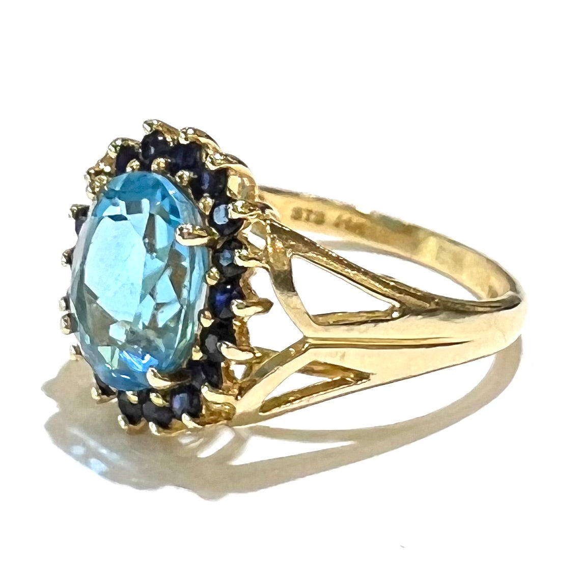 Yellow gold ring prong set with swiss blue topaz center stone and a halo of blue round blue sapphires.